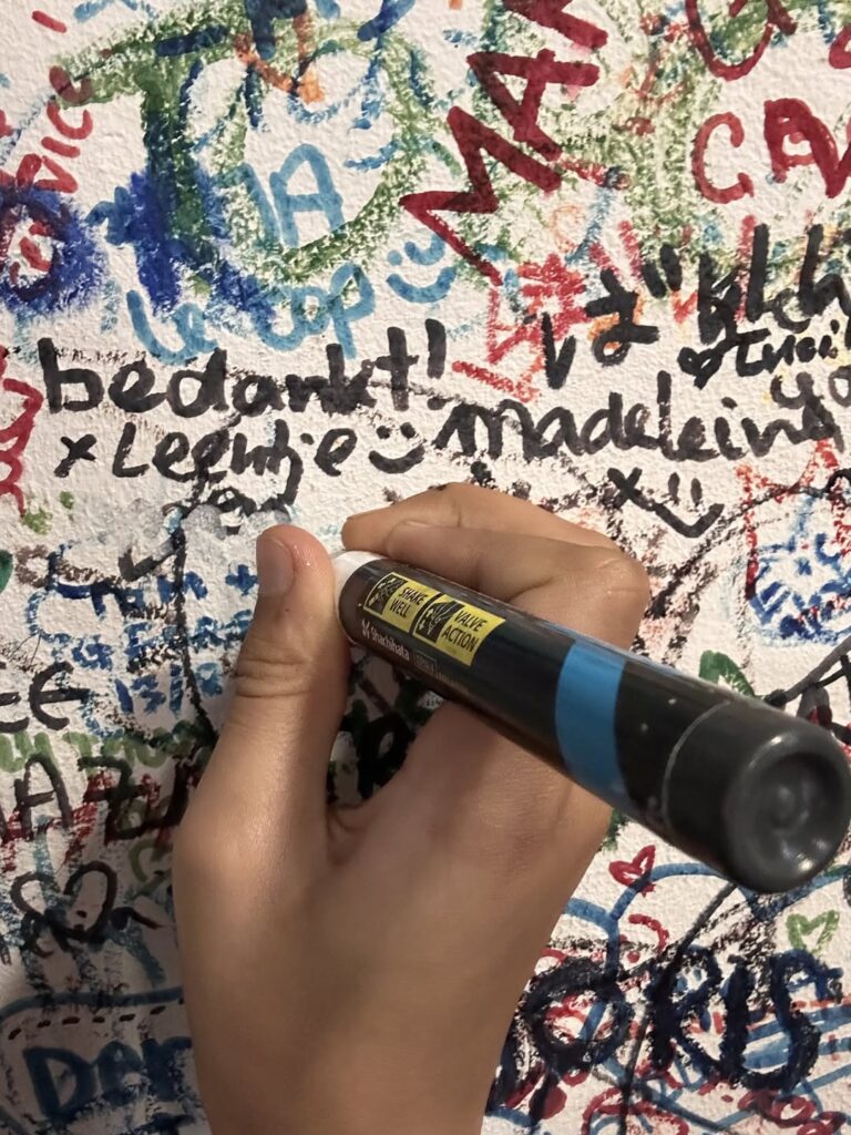 Childs hand holding pen writing on wall covered in writing
