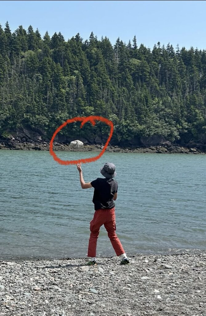 Child joyfully throwing a heavy rock into the water, showing natural sensory play.